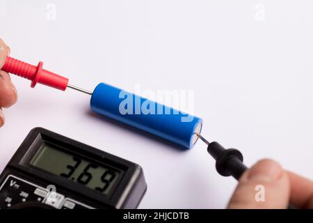 18650 blue battery, multimeter red and black poles in the hands of man checking voltage and amps with white background, Stock Photo
