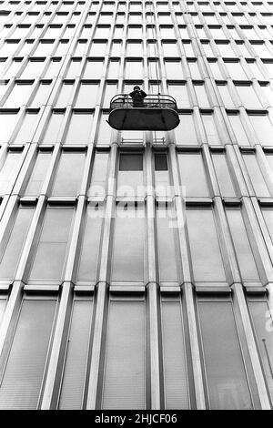 Stockholm in the 1960s. A man in a moving basket is seen outside the fasade of one of the high-rise buildings in central Stockholm, the so called Hötorgsskraporna. The basket is more or less a lift going up and down as you chose and works like general maintanance and window cleaning were performed from it. Sweden 1964 Kristoffersson ref 3-53 Stock Photo