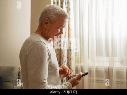 Retired male chatting with friends in social media, typing on smartphone. Happy senior man using phone at home. Stock Photo