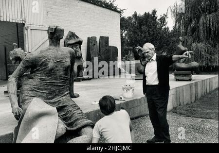 Sir Henry Spencer Moore instructs an assistant outside his home studio in Much Hadham, England, 1970. Moore was an English-born artist and sculptor, known for his modernist, abstract works. Born 1898, died 1986. Stock Photo