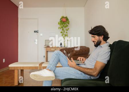 Young business man working at home from his living room couch with laptop on his lap. Gray notebook for working. Home office concept. High quality pho Stock Photo