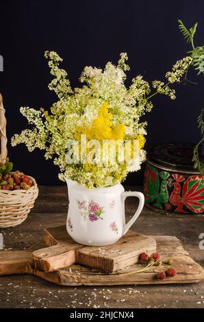 Still life with a bouquet of summer wildflowers of the bedstraw in a white jug on an old vintage wooden table. Stock Photo