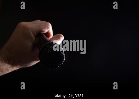 Male singer hand holding black microphone close up, on black background with copy space. Stock Photo