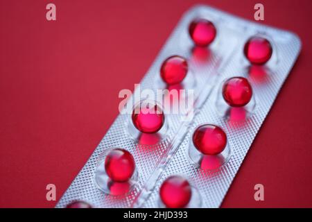 Red round pills vitamins capsules in a blister pack on a red table. Stock Photo