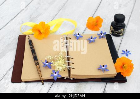 Writers block and out of ideas concept with old leather notebook with open blank pages, old fashioned pen, ink bottle and flora. Stock Photo