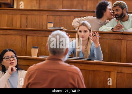 Multicultural students looking at blurred professor during lecture in university Stock Photo