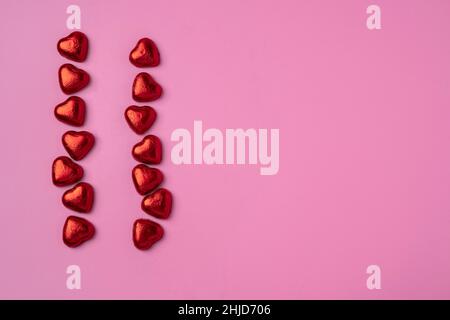 Two Streams of hearts on Bright Festive Pink background with shiny candies in the shape of hearts wrapped in foil. Beautiful background for a postcard Stock Photo