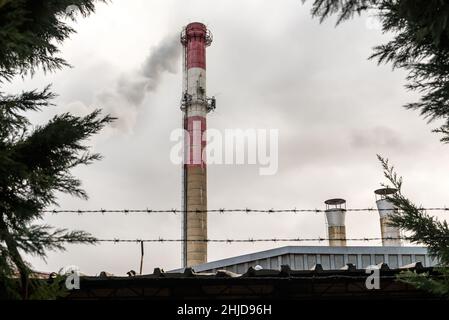 Air pollution by smoke coming out of a large factory chimney. A close-up of smoke coming out of chimneys against the cloudy grey sky. Air pollution co Stock Photo