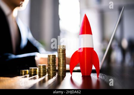 Red Rocket Besides Stacked Coins And Arrow Showing Upward Direction Stock Photo