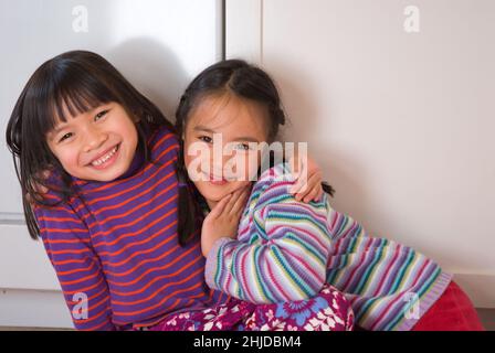 Two five year old girls hugging, friends since infancy, smiling, looking at camera Stock Photo
