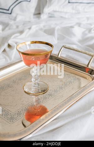 single vintage glass of pink rose wine on silver tray on white bedsheets Stock Photo