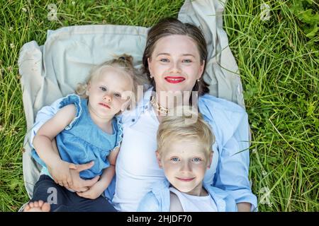 Little brother and sister and mother lie on grass. View from above. Happy family. Stock Photo