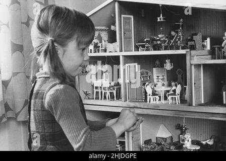 Playing in the 1970s. A little girl is playing with her dolls house that is decorated with nice furniture and dolls. Sweden 1973 Stock Photo