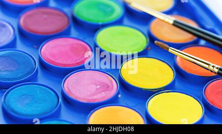 Palette with paints and brushes macro photo. Close-up watercolor paints. The concept of drawing and painting pictures. Drawing courses concept. Stock Photo