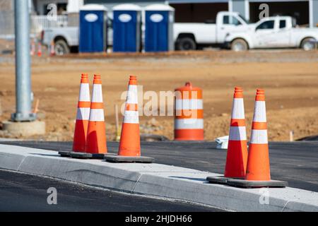 Horizontal shot of a group of orange traffic cones in front new apartment construction.  Three porta potties in the background. Stock Photo