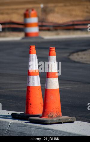 Vertical close-up shot of traffic cones with a traffic barrel in the background at new parking lot construction.  Barrel is slightly out of focus on p Stock Photo