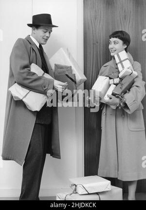 Christmas in the 1950s. A couple with christmas gifts after a shopping tour returning to their home and struggles a bit with the key to the door. 1953 Stock Photo