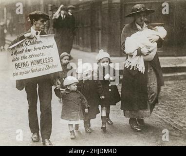 Poverty in october 1919. A family is seen walking on Fleet Street in London and the man is holding a sign with the text 'My wife, 5 children & myself have been turned into the streets. Being homeless, can any one find us a shelter.' The mother carries an infant child and the other four walks along for themselves. The family being evicted from their apartment in Kensington London. Montague Channell, father and husband and his wife Mabel has taken the step to manifest their situation in the busy newspaper Fleet Street in London carrying the message. Stock Photo