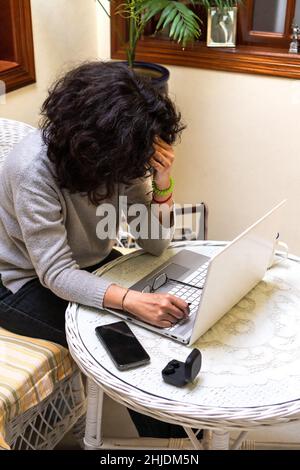 From above of unrecognizable tired female freelancer with curly dark hair touching forehead while working remotely on laptop in cafe Stock Photo