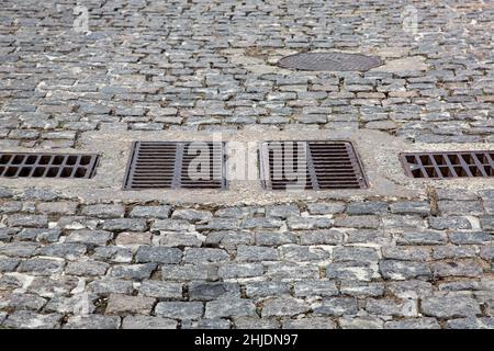 cobblestone granite stone road with drain grates for stormwater drainage urban streets improvement in the old European town close-up, nobody. Stock Photo