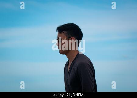 Palomino, Dibulla, La Guajira, Colombia - December 4 2021: A Young Latin Man Wearing Sunglasses Against a Backdrop of Clear Sky Stock Photo