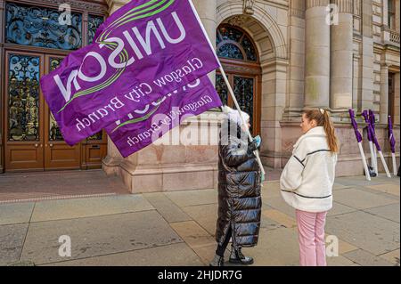 Glasgow, UK. 27th Jan, 2022. A member of the workers union Unison is seen holding a flag while speaking with a reporter during the protest.Following the October 23rd protest in 2018, female employees of Glasgow City Council are still having issues with receiving the money owed to them, with some even saying the council is refusing to pay up, the payout tops £500m. Credit: SOPA Images Limited/Alamy Live News Stock Photo