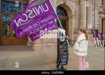 Glasgow, UK. 27th Jan, 2022. A member of the workers union Unison is seen holding a flag while speaking with a reporter during the protest.Following the October 23rd protest in 2018, female employees of Glasgow City Council are still having issues with receiving the money owed to them, with some even saying the council is refusing to pay up, the payout tops £500m. (Photo by Stewart Kirby/SOPA Images/Sipa USA) Credit: Sipa USA/Alamy Live News Stock Photo