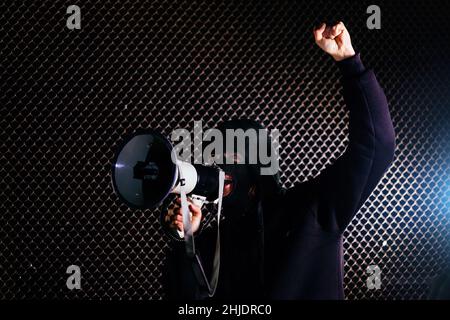 Angry masked man is shouting into the megaphone. Stock Photo