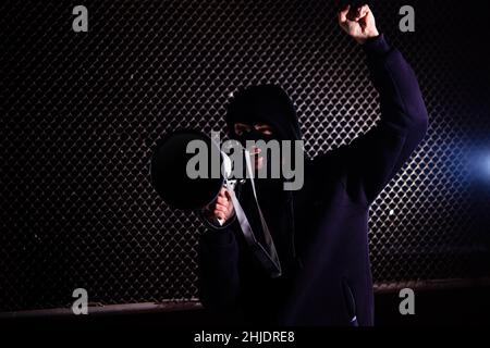 Angry masked man is shouting into the megaphone. Stock Photo