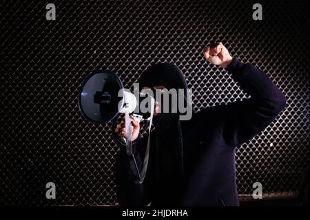 Angry masked man is shouting into the megaphone. Stock Photo