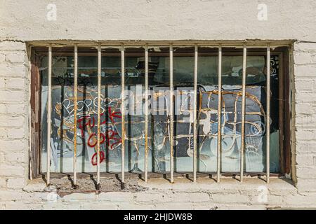 Graffiti painted on barred window set in white painted brick wall of an old building in downtown Santa Barbara, California. Stock Photo
