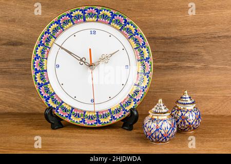 Famous Thai porcelain called Benjarong design as a beautiful clock and small jar with lid on wooden table. Benjarong is Thai porcelain design in five Stock Photo