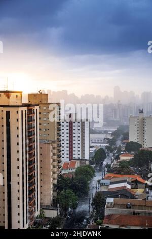 Residential apartment blocks and low-rise housing. Street wet with rain. Dramatic sky with sun and dark rain clouds. São Paulo, Brazil Stock Photo