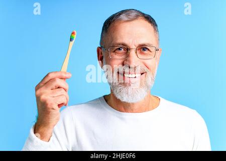 man showing multi colored rainbow tooth brush in blue background studio Stock Photo