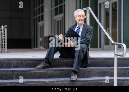 Successful old businessman sitting on a staircase by an office building Stock Photo