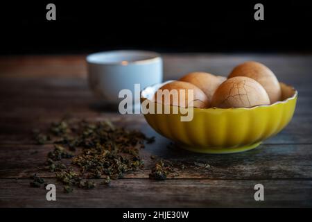 Hard boiled Chinese marble spiced tea eggs on rustic wooden table with tea leaves and cup of Chinese tea in background. Stock Photo