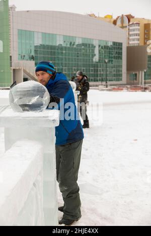 A sculptor carves a round ice ball out of a block of ice with a chisel ...