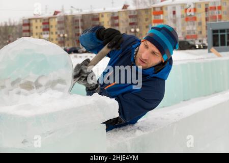 A sculptor carves a round ice ball out of a block of ice with a chisel ...