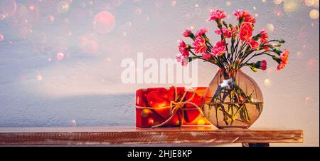 Flowers in a vase and a gift with red wooden hearts on the table Stock Photo