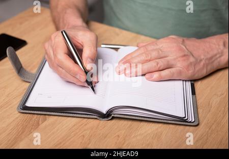 Male hands taking notes, writing plans in notebook or planner. Planning in schedule diary, close up. Starting from scratch concept. Stock Photo