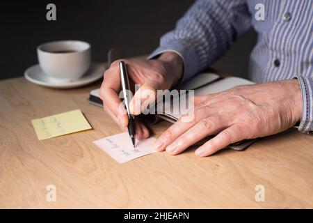 Businessman hands writing memo notes or reminder on sticker at office desk. Stock Photo