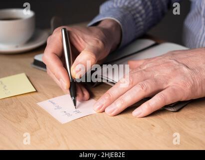 Businessman hands writing memo notes or reminder on sticker at office desk. Stock Photo