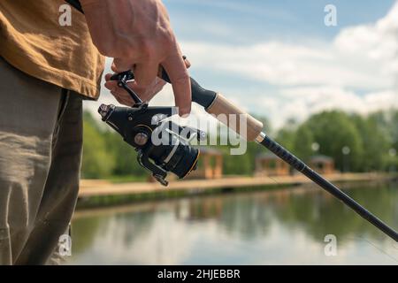 Fisherman hands holding and rotating spinning reel rod and fishing over river, close up. Stock Photo