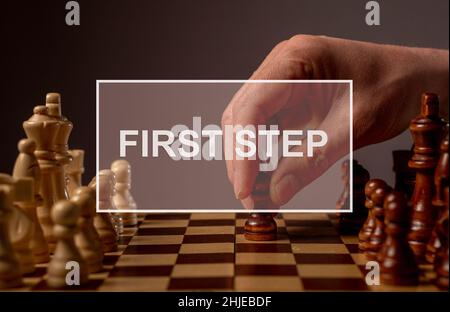 First step forward in business concept. Inscription on image with hand moving pawn on chessboard, starting game and making first step. Stock Photo