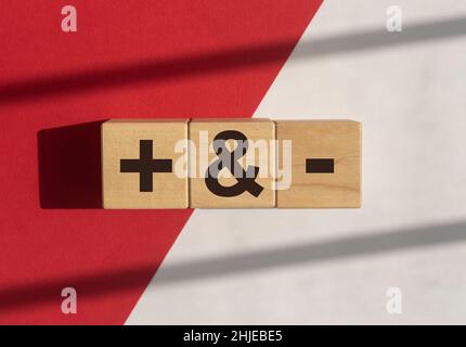 Plus and minus signs on wooden dices on white and red background with daylight. Concept of positive and negative, pros and cons. Stock Photo