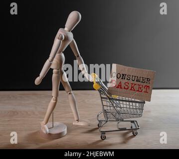 Consumer basket text in shopping cart pushed by wooden doll. Stock Photo