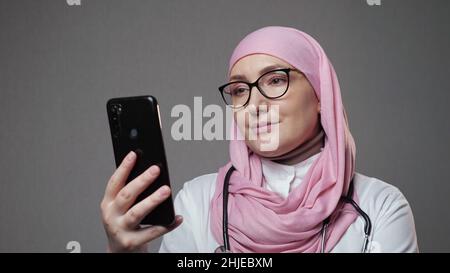 Muslim female doctor smiles surfing internet via phone Stock Photo