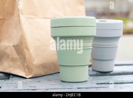 https://l450v.alamy.com/450v/2hjec1b/two-collapsible-eco-cups-and-craft-parcel-on-city-park-bench-reusable-sustainable-silicon-mugs-for-takeaway-tea-or-coffee-2hjec1b.jpg