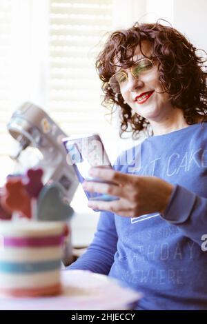 Smiling caucasian woman taking a picture of a cake with her mobile phone. Selective focus. Stock Photo