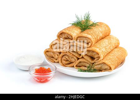 A stack of thin stuffed pancakes with dill, sour cream and red caviar isolated on a white background. Side view, close-up. Traditional Russian pancake Stock Photo